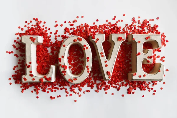 Wooden letters forming word LOVE lying on white surface and sprinkled with red confetti