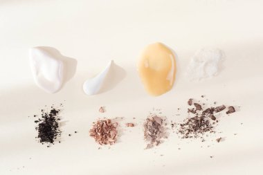 Bej ve kahverengiye boyanmış göz farı, açık arkaplanda yüz kremi örnekleri. Dekoratif makyaj konsepti. Minimalizm.