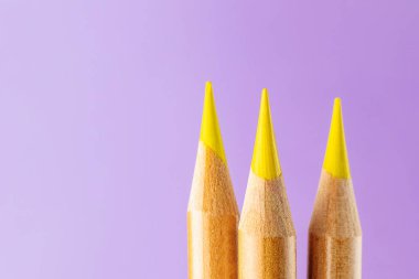 Leylak arkaplanına yakın plan üç sarı kalem. Çizim, eğitim ve sanat terapisi için malzeme kavramı. Minimalizm, metin için yer.