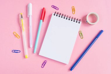 Kalemler, ataçlar, defter ve pembe arka plandaki diğer kağıtlar. Metnin yeri, minimalizm. Okul, ofis, eğitim kavramı.