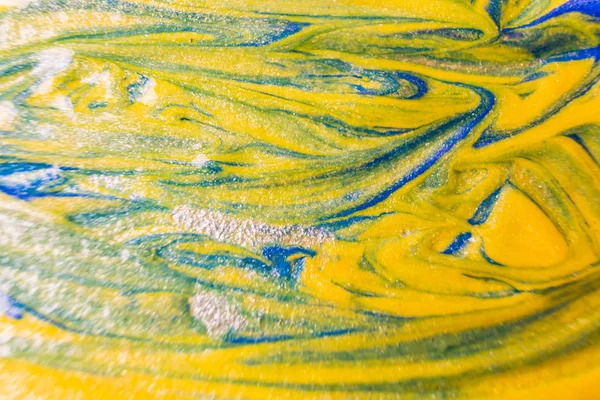Macro photo. Paint of yellow and blue shades close up. Abstract bright image of acrylic paint. The concept of drawing, art therapy. Mother of pearl background.