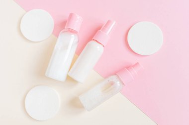 Kozmetik sünger ve pembe arka planda emülsiyonu olan şişeler. Yüz ve vücut bakımı kavramı, kozmetoloji. Minimalizm, üst görüş. Metin için boşluk