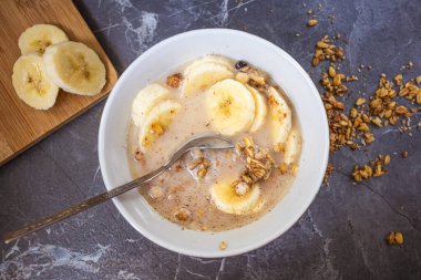 Çikolatalı müsli ve koyu gri mermer bir masada taze muz. Tabakta bir kaşık da var. Tahta kesme tahtasının üzerinde muzlar var. Sağlıklı yemek ve sağlıklı kahvaltı kavramı.. 