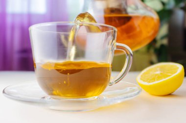 Hot herbal tea from a teapot is poured into a transparent cup. Nearby lies a lemon. The concept of healthy organic drinks.
