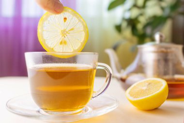 A lemon is placed in a cup of herbal tea. Transparent cup. In the background is a teapot. The concept of healthy organic drinks.