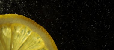 Karanlık bir arka planda sulu bir dilim limon. Çerçevede, turunçgilin sadece bir kısmı. Uzun afiş. Havaya bir damla su. Ayrıntılı makro fotoğraf. Boşluk, minimalizm.