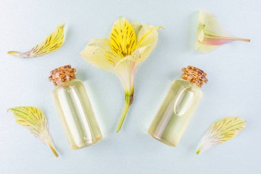 Aromaterapi konsepti, spa. Pastel mavi arka planda çiçek yağı ve sarı çiçek yaprakları olan şişeler. Parlak renklerle bembeyaz yatıyordu. Kopyalama alanı, minimalizm, üst görünüm.