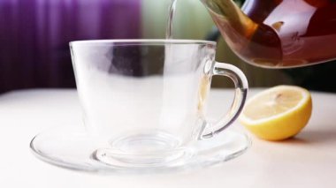 Hot herbal tea from a teapot is poured into a transparent cup. Nearby lies a lemon. The concept of healthy organic drinks.