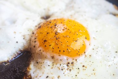 Fried egg close-up: whole yolk in focus. The concept of fried food, breakfast. Egg sprinkled with pepper.