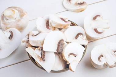 Ahşap bir arka planda tahta bir kasenin içinde ve etrafında dilimlenmiş çiğ chapminonlar. Sağlıklı gıda, vejetaryenlik, mantar kavramı..