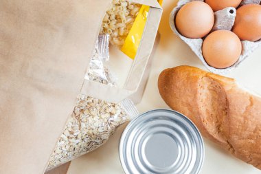 Kağıt el çantası ve çeşitli ürünler. Mısır gevreği, yumurta, konserve yiyecek. Yemek bağışı, teslimat hizmeti konsepti. Üst görünüm, telif alanı. İzolasyon dönemi için gıda stoku.
