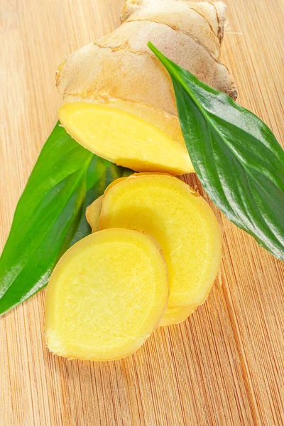 Sliced ginger root and green leaves on a wooden board. The concept of a healthy food, a cure for the common cold, flavoring.