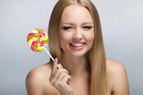 Милая молодая женщина смотрит в камеру и держит леденец. Положительные человеческие эмоции. Смех
