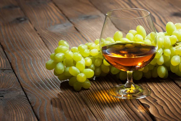 Verre de cognac et bouquet de raisins sur une table en bois . — Photo