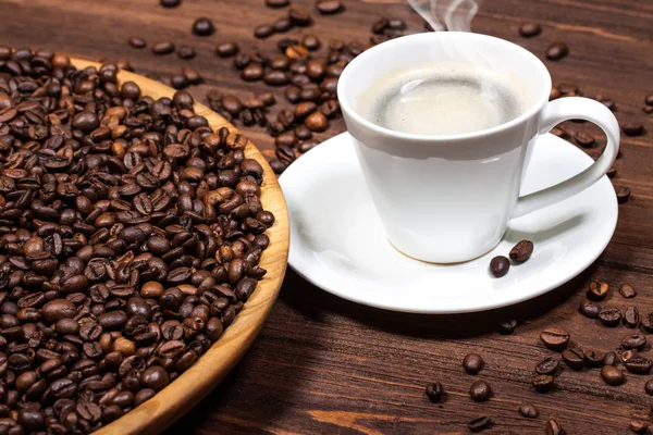 Bir fincan kahve ahşap bir masa üzerinde. Büyük bir tabak içinde kahve çekirdekleri. — Stok fotoğraf