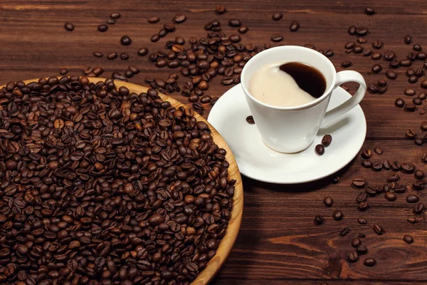 A cup of coffee on a wooden table. Coffee beans in a large dish. — Stock Photo, Image