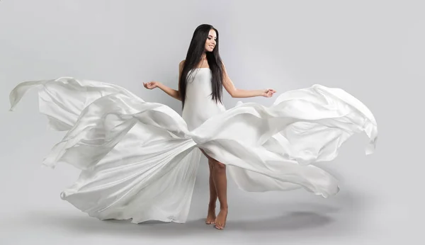 Mooi jong meisje in een witte jurk vliegen. Vloeiende weefsel. Lichte witte doek vliegen in de wind — Stockfoto
