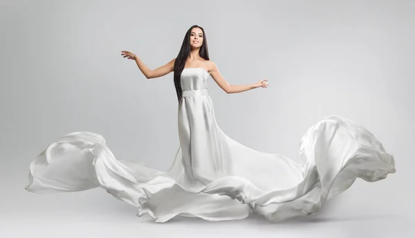 Mooi jong meisje in een witte jurk vliegen. Vloeiende weefsel. Lichte witte doek vliegen in de wind — Stockfoto