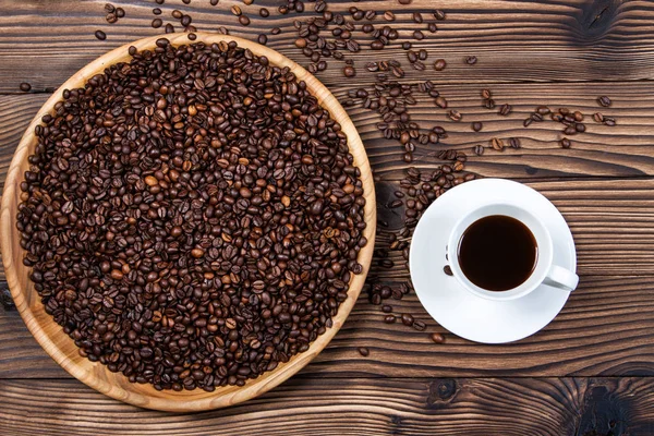 Coffee beans on a large plate and a cup of coffee on a wooden ta — Stock Photo, Image
