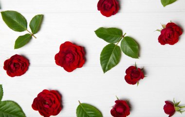 Kırmızı gül ve yaprakları yapılmış çiçek deseni. Beyaz ahşap tabl