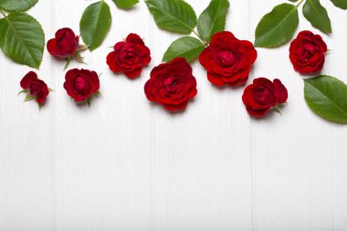Kırmızı güller ve Beyaz ahşap bir masa üzerinde yeşil yaprakları. Vintage çiçek desenli. Yukarıdan görüntüleyin. Çiçek deseni. Metin için boş yer