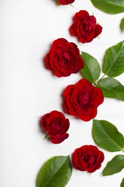 Kırmızı güller ve Beyaz ahşap bir masa üzerinde yeşil yaprakları. Vintage flor