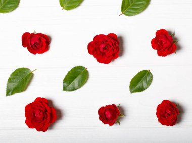 Kırmızı gül ve yaprakları yapılmış çiçek deseni. Beyaz ahşap masa. Yukarıdan görüntülemek