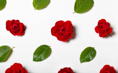 Kırmızı gül ve yaprakları yapılmış çiçek deseni. Beyaz ahşap masa. Yukarıdan görüntülemek