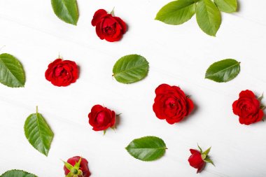Kırmızı gül ve yaprakları yapılmış çiçek deseni. Beyaz ahşap masa. Yukarıdan görüntülemek