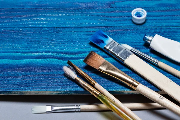 Krásné dřevěné pozadí vybarvené světle modré barvy. Otevřete tubu barvy a štětce — Stock fotografie