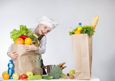 mutlu kız şapka şef çuval dolusu yiyecek ile. Taze meyve ve sebze masada torbalarda çeşitli. Sağlık gıda.