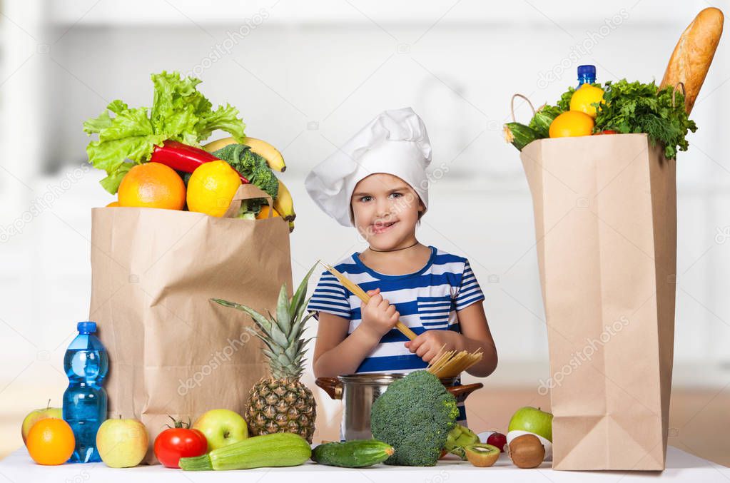 Happy little girl in the hat of the chef with big bags of food. A