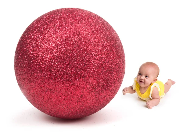 Bebê bonito olhando para um enorme ornamento de Natal no branco — Fotografia de Stock