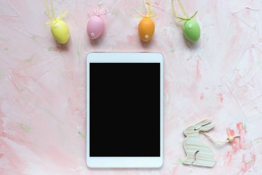 Pembe arka planda çok renkli yumurta süslemesi ve tablet. Paskalya konsepti.