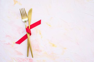 Pembe arka planda kırmızı kurdeleli altın çatal bıçak takımı.