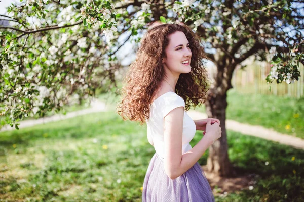 Fröhliche junge Frau im weißen T-Shirt unter dem blühenden Baum. — Stockfoto