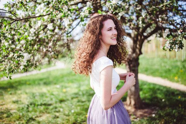 Cheerful young woman in a white t-shirt under the blooming tree.