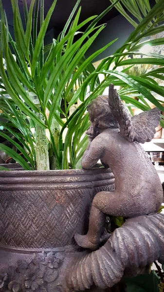 Cupid or baby angel resting on edge of planter with plant