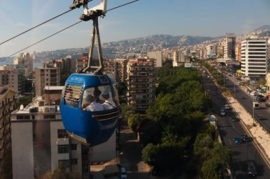 Jounieh, Lübnan - 13 Mayıs 2017: Yerliler Jounieh otoyolunun üzerindeki bir teleferik ve arka plandaki şehir manzarası ile işe gidip geliyorlar.