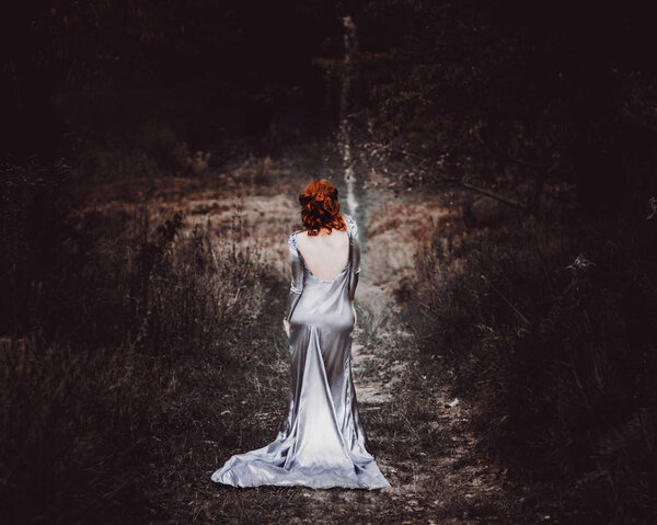 Ginger hair, red hair, girl in long silver beautiful gray dress, backless dress, background for books or stories, woman staying on trail in dark forest,