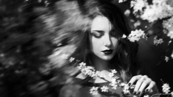 Abstract portrait, girl face with dark lips and downcast eyes, woman in blooming garden, sad and calm, black and white photo, art photography, concept of fantasy and mystical
