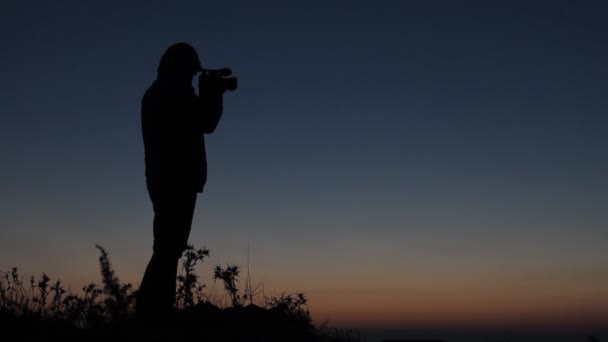 Silhouette Mann steht im Sonnenuntergang auf Berg mit Camcorder — Stockvideo