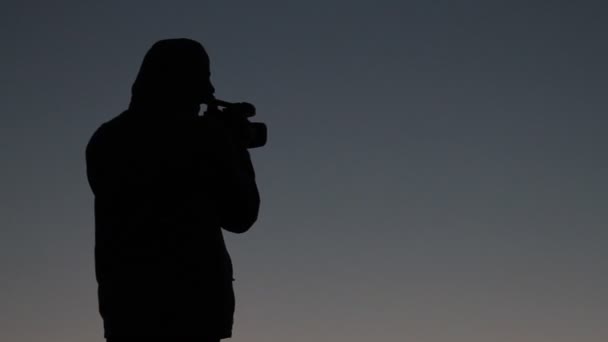Siluett man i solnedgången på berg med videokamera — Stockvideo