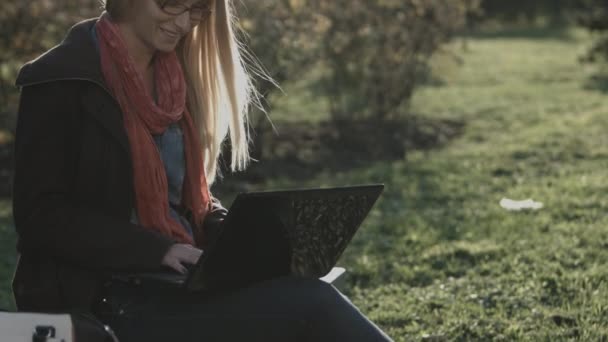 Vacker kaukasiska flicka arbetar på bärbar dator i stadsparken — Stockvideo