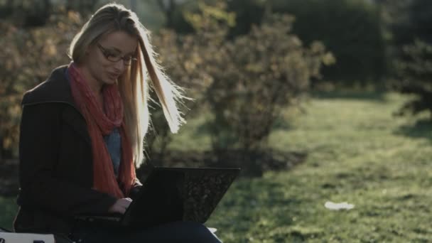 Beautiful Caucasian girl working on laptop in city park — Stock Video