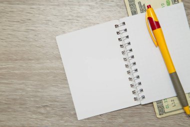 Bir boş defter sayfası ve ahşap ofis masaları dolar kalemle. Kopya alanı ile Üstten Görünüm.