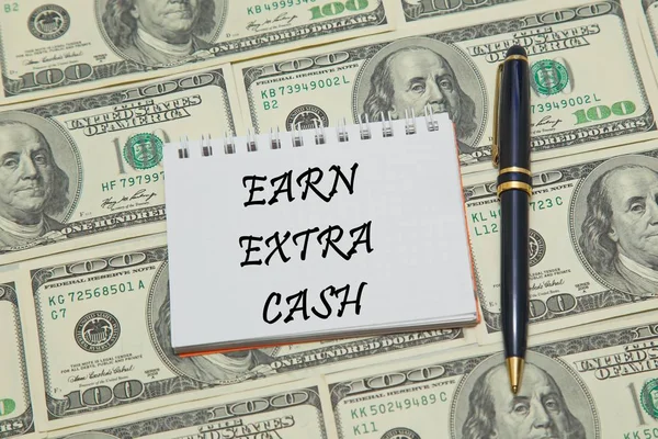 Page de carnet avec texte EARN EXTRA CASH sur fond dollar — Photo