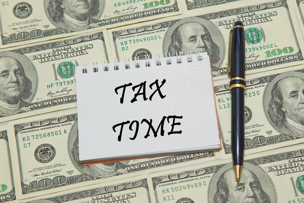 Página de caderno com texto TAX TIME em fundo dólar — Fotografia de Stock