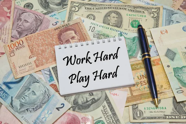 Pagina del taccuino con testo WORK HARD, PLAY HARD, sfondo da diverse valute del mondo — Foto Stock