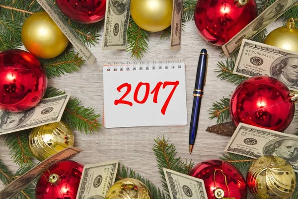 Kerstdecoratie met dollars en tekst in notitieblok 2017 op houten tafel — Stockfoto